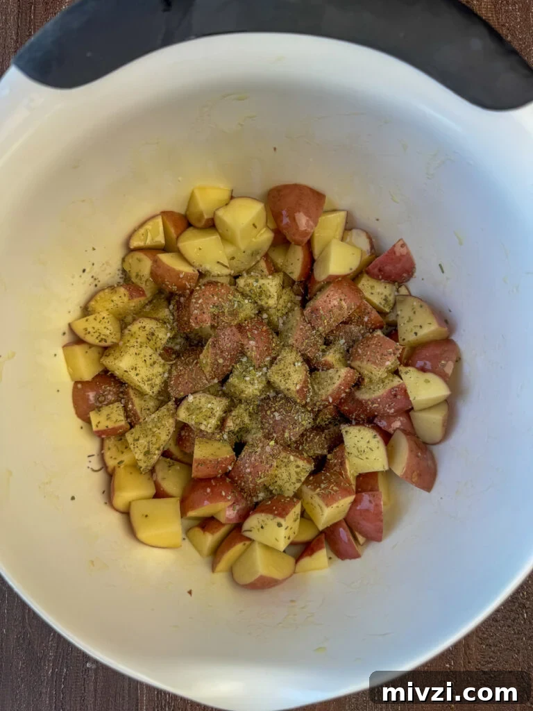Chunks of potatoes in a bowl tossed in olive oil and coated in seasonings.