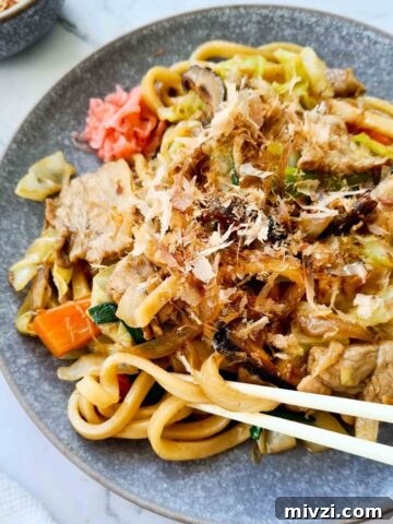 Side view of a plate of udon stir fry with chopsticks