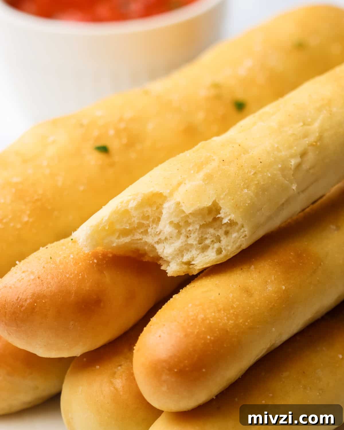 Crispy Homemade Breadsticks Recipe for Perfect Dinner Sides 3 a stack of breadsticks, one with a bite taken out of it