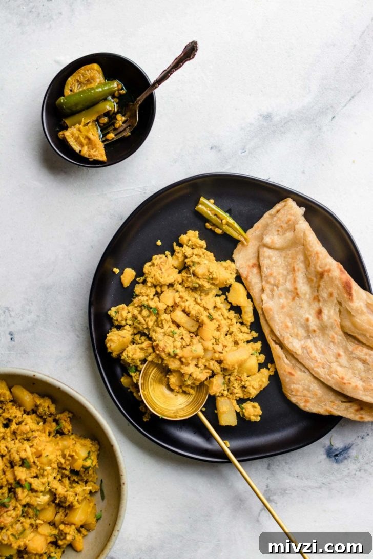 Spiced Potato and Egg Bhurji (Aloo Anday Ki Bhujia) 2 Scrambled Egg and Potatoes and paratha on a black plate with a gold spoon