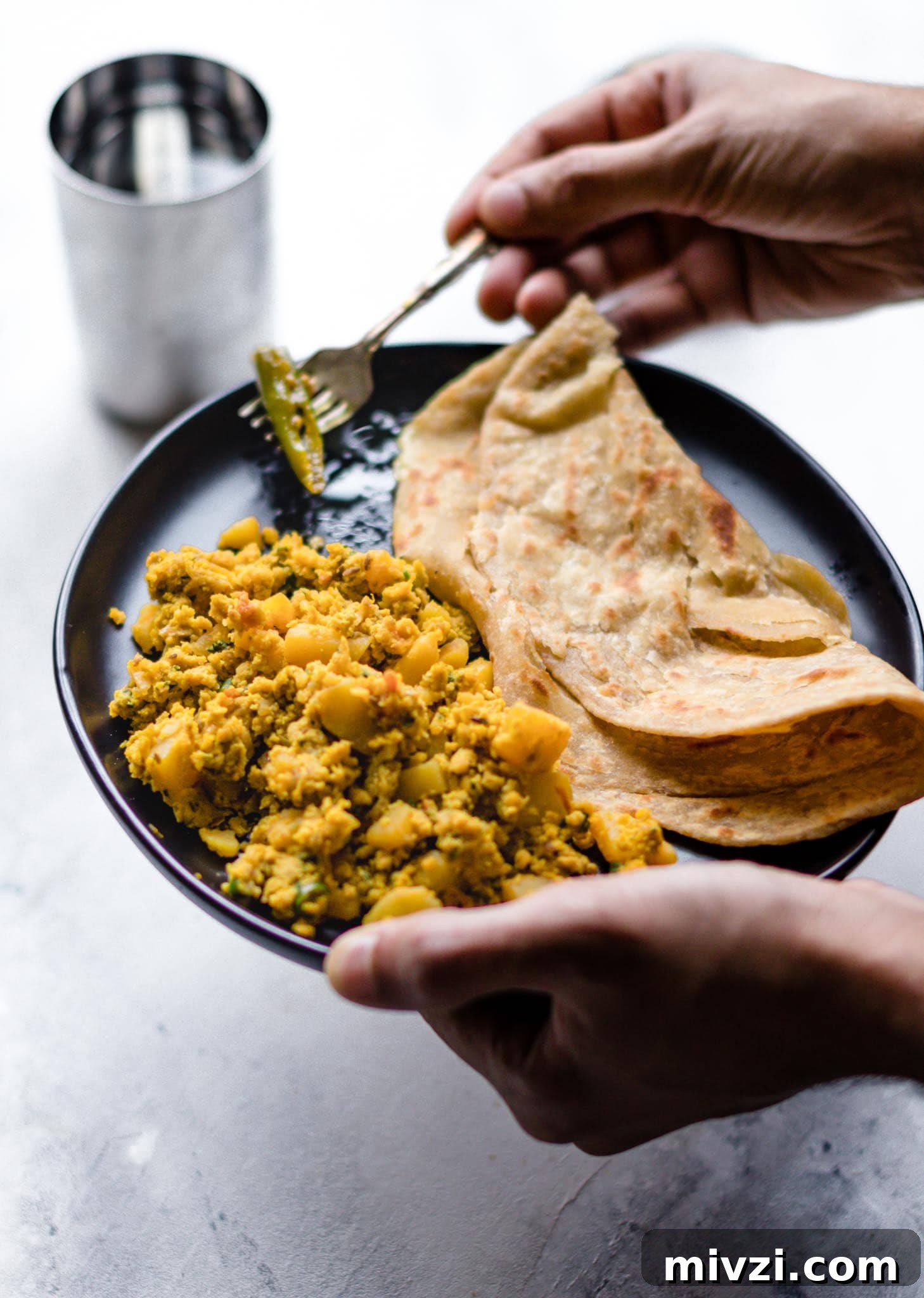 Spiced Potato and Egg Bhurji (Aloo Anday Ki Bhujia) 5 Holding a fork and a plate of scrambled egg and potatoes with paratha