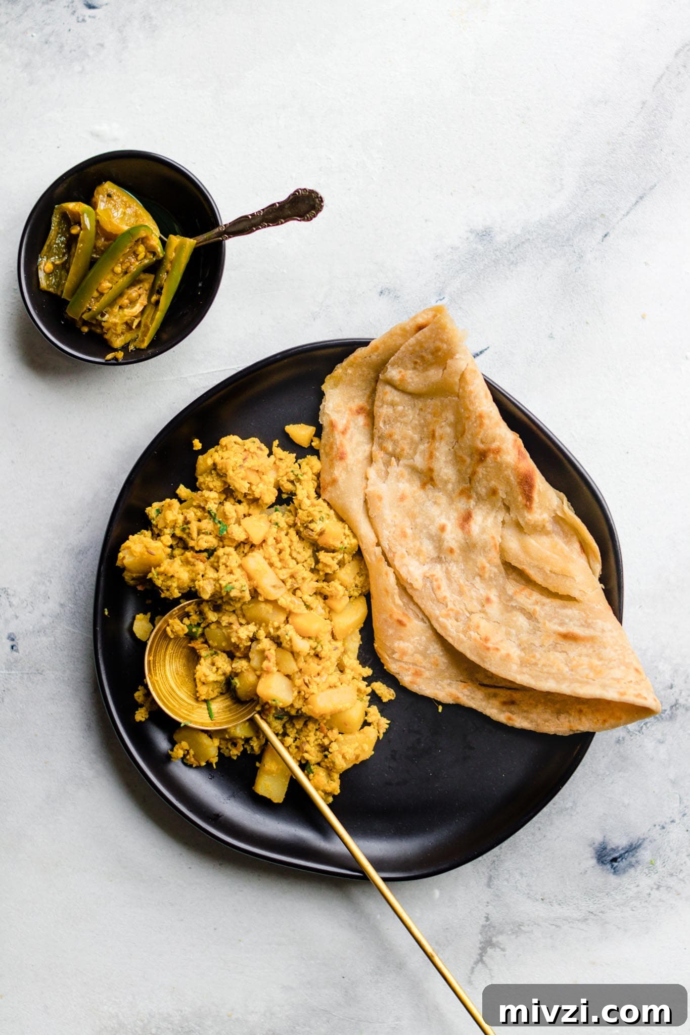 Spiced Potato and Egg Bhurji (Aloo Anday Ki Bhujia) 6 Scrambled Egg and Potato Curry with Paratha on a black plate with a side of achaar (mixed pickle)