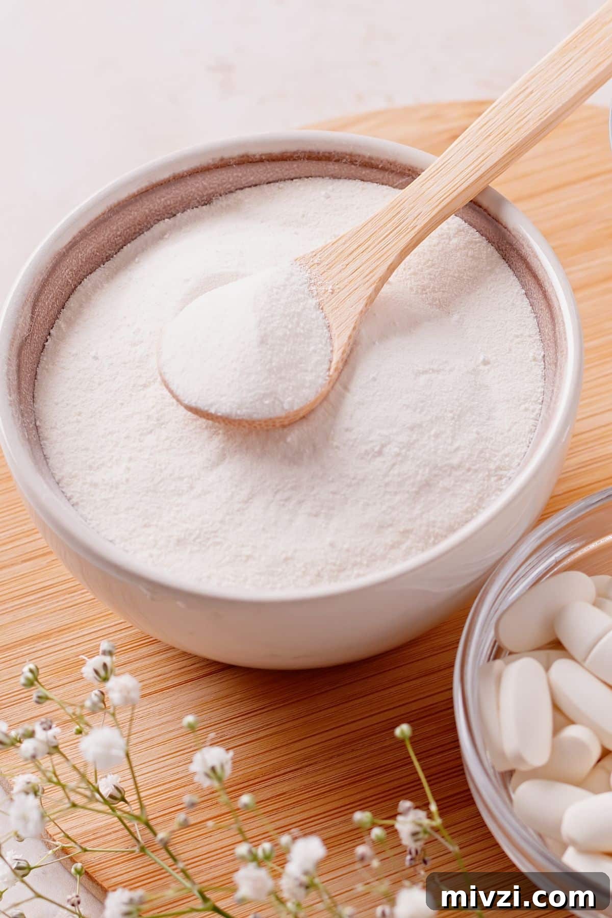 Bowl of powdered collagen with a wooden spoon and pills of collagen next to it.