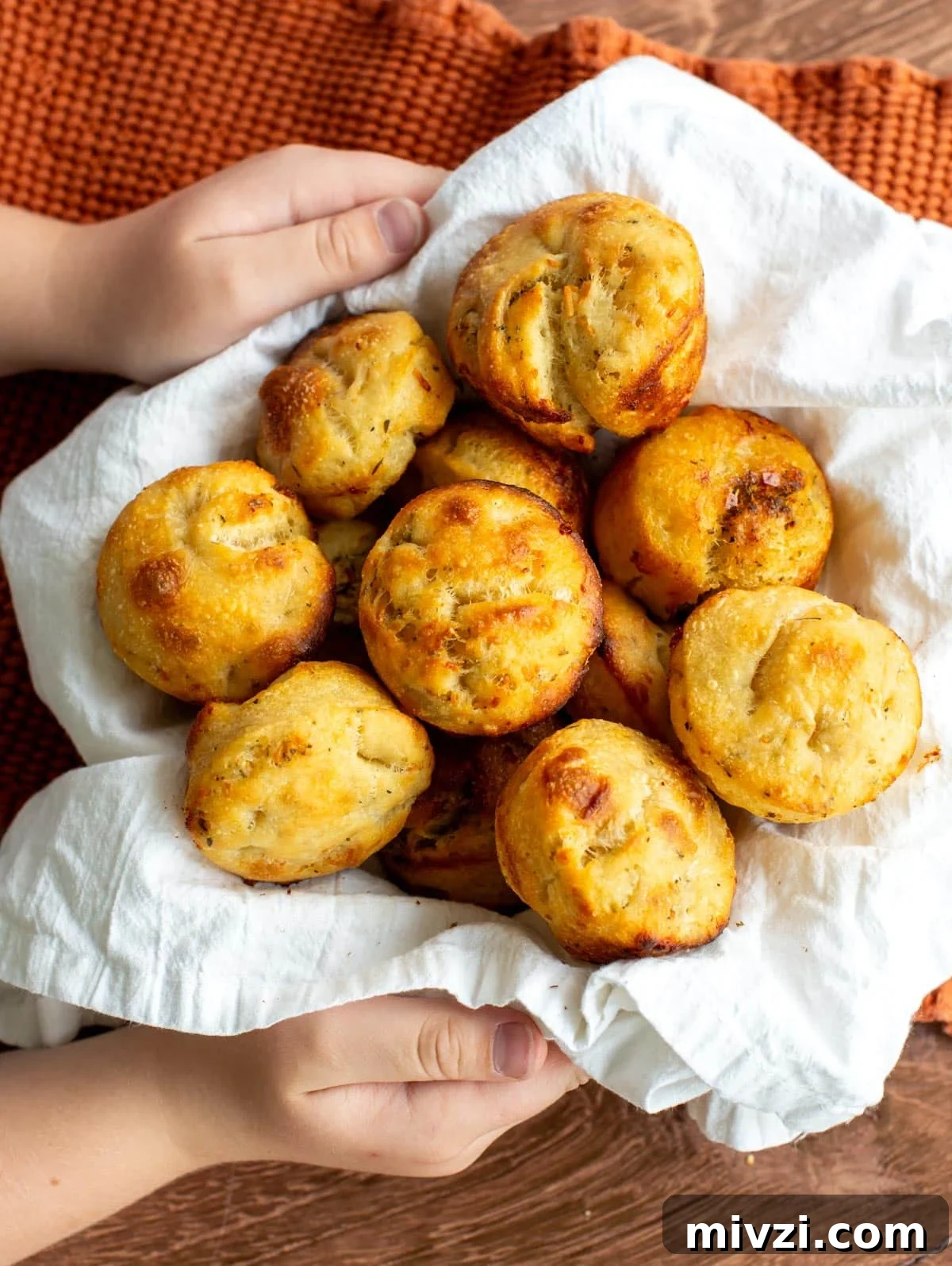 A bowl of sourdough focaccia rolls being held by two hands.