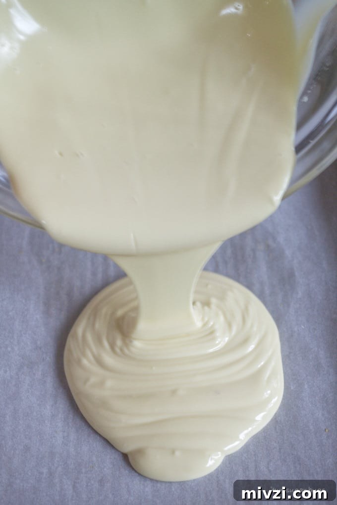 Cookie Butter White Chocolate Bark Recipe | Crunchy Cookie Butter Bark 8 melted white chocolate being poured onto a baking pan