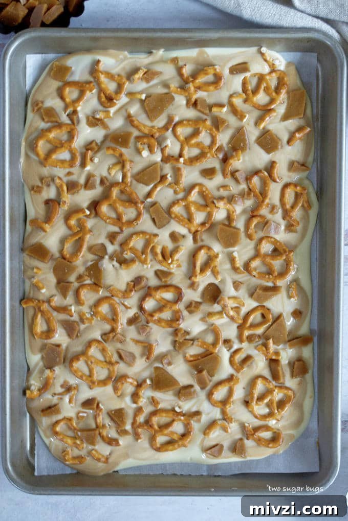 Cookie Butter White Chocolate Bark Recipe | Crunchy Cookie Butter Bark 10 melted white chocolate and cookie butter spread on a baking sheet with pretzels and toffee