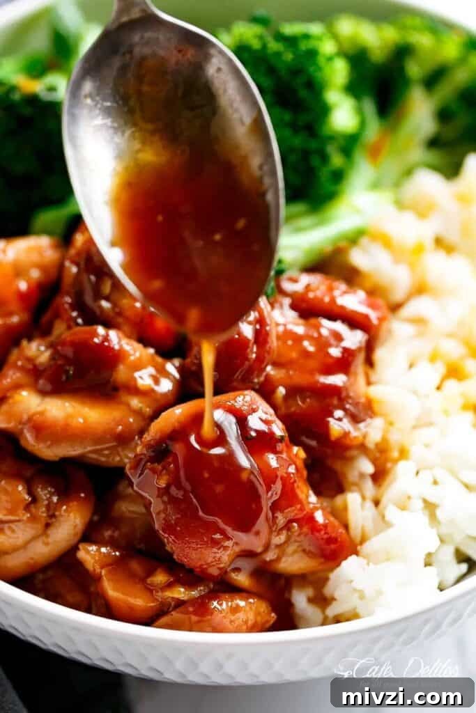 Close-up image of teriyaki chicken served in a white bowl, accompanied by teriyaki sauce, rice, and broccoli.