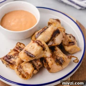 Grilled nuggets on a white plate with a bowl of sauce.
