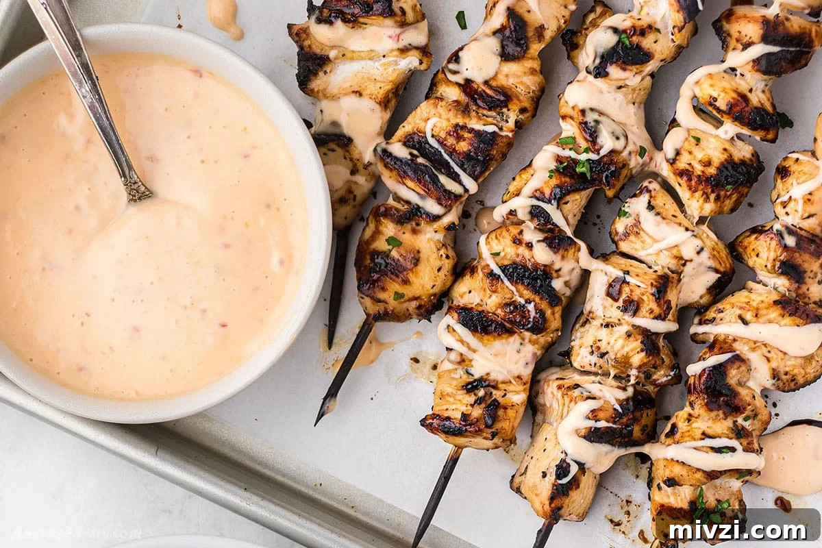 Spicy Bang Bang Chicken Skewers Recipe for Grilled Poultry 9 An overhead image of bang bang chicken skewers on a sheet pan with a bowl of sauce on the side.