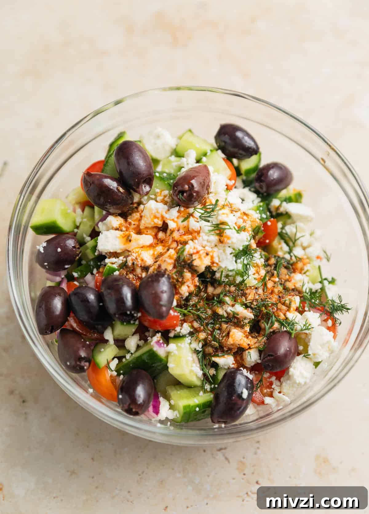 Mediterranean-Style Grilled Chicken with Lemon and Herbs 6 Cucumbers, olives, tomatoes, feta and dressing in glass bowl before tossing.