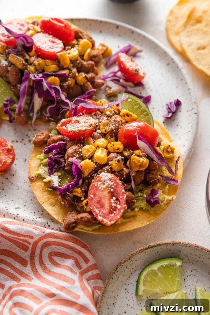 Pinto Bean Tostadas with Fresh Tomato and Corn Salsa 2 Small plate with a pinto bean tostada topped with a street corn tomato salsa, crumbled Cotija cheese, and shredded cabbage.