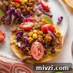 Pinto Bean Tostadas with Fresh Tomato and Corn Salsa 9 Small plate with a pinto bean tostada topped with a street corn tomato salsa, crumbled Cotija cheese, and shredded cabbage.