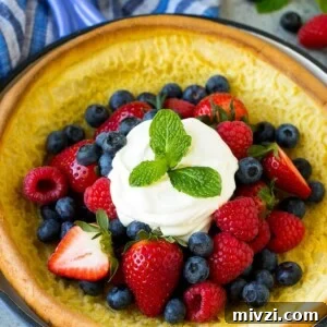 A Dutch baby puffed pancake in a skillet, topped with berries and whipped cream.