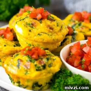 Breakfast egg muffins on a serving plate garnished with tomato and herbs.