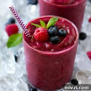 A glass of frozen fruit smoothie in crushed ice, garnished with berries and mint.