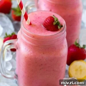 A mason jar mug of strawberry banana smoothie with fresh strawberry on top.