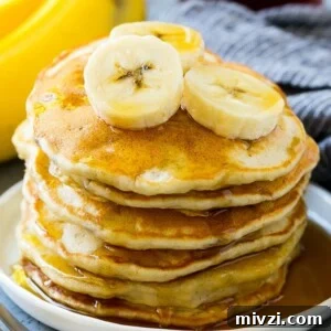 A stack of banana pancakes with banana slices and maple syrup.
