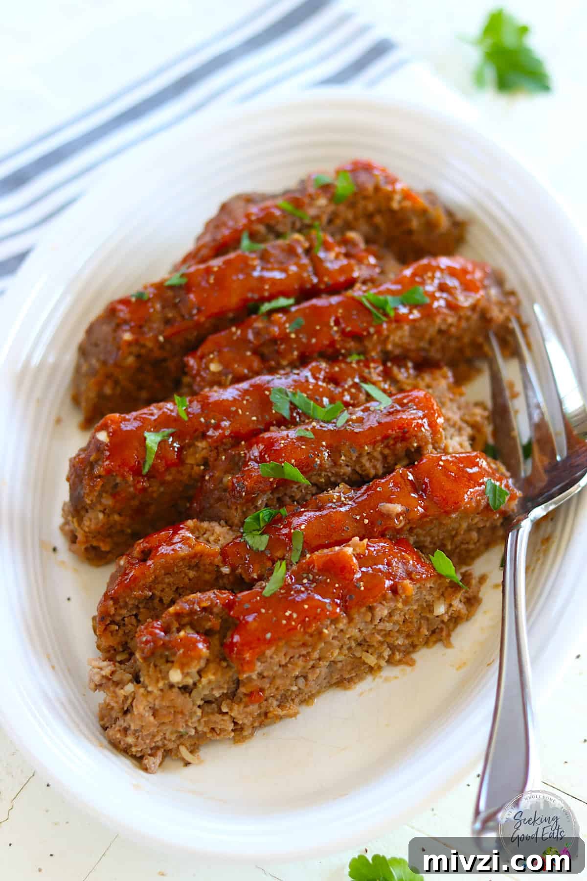Sliced meatloaf on a white plate garnished with parsley.
