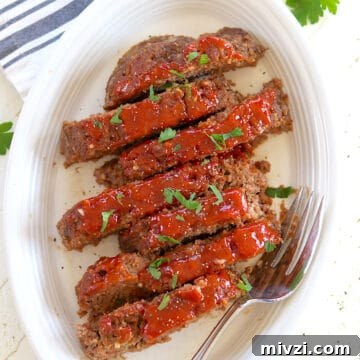 Ketchup and brown sugar sauce coat sliced of cooked meatloaf on a white platter.