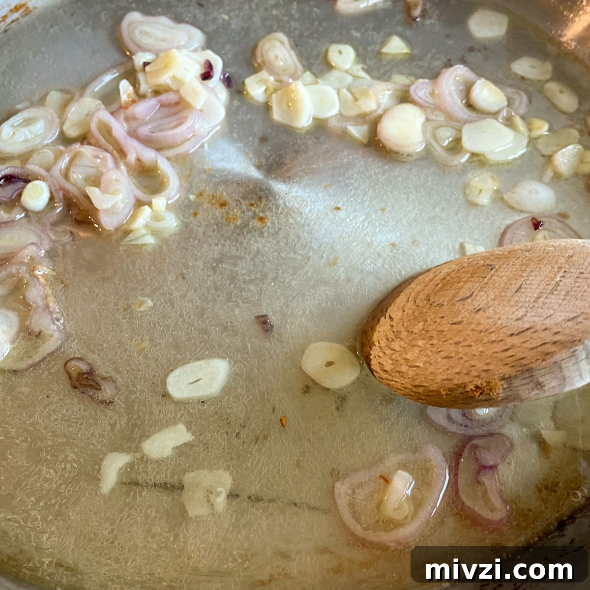 Sautéed shallots and garlic are shown in a stainless steel pan with white wine and lemon juice.