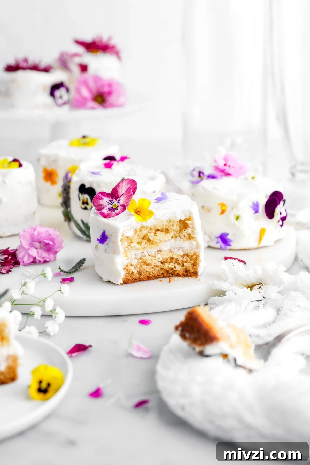 bite missing from mini honey orange blossom cake on marble tray with more mini cakes behind and edible flwoers.