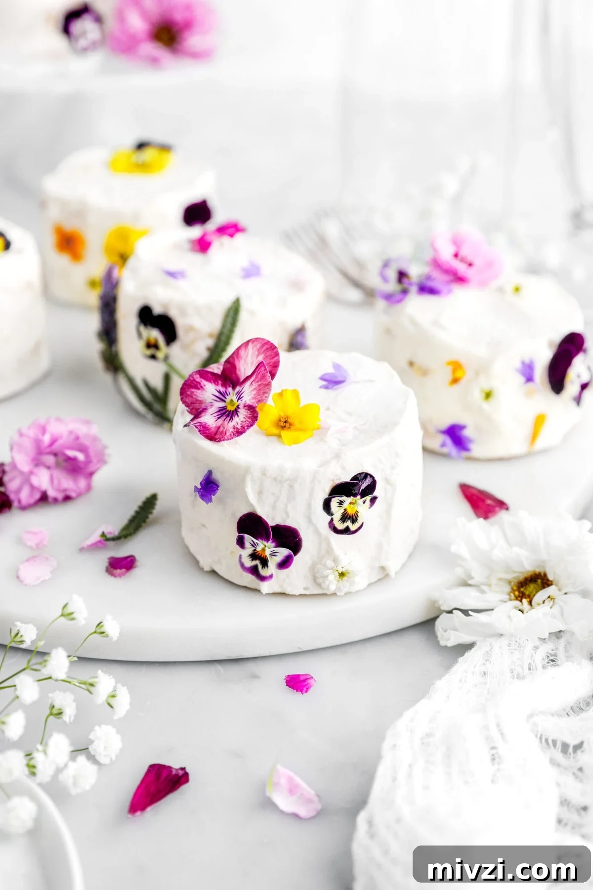 angled close up of frosted mini cake decorated with edible flowers.