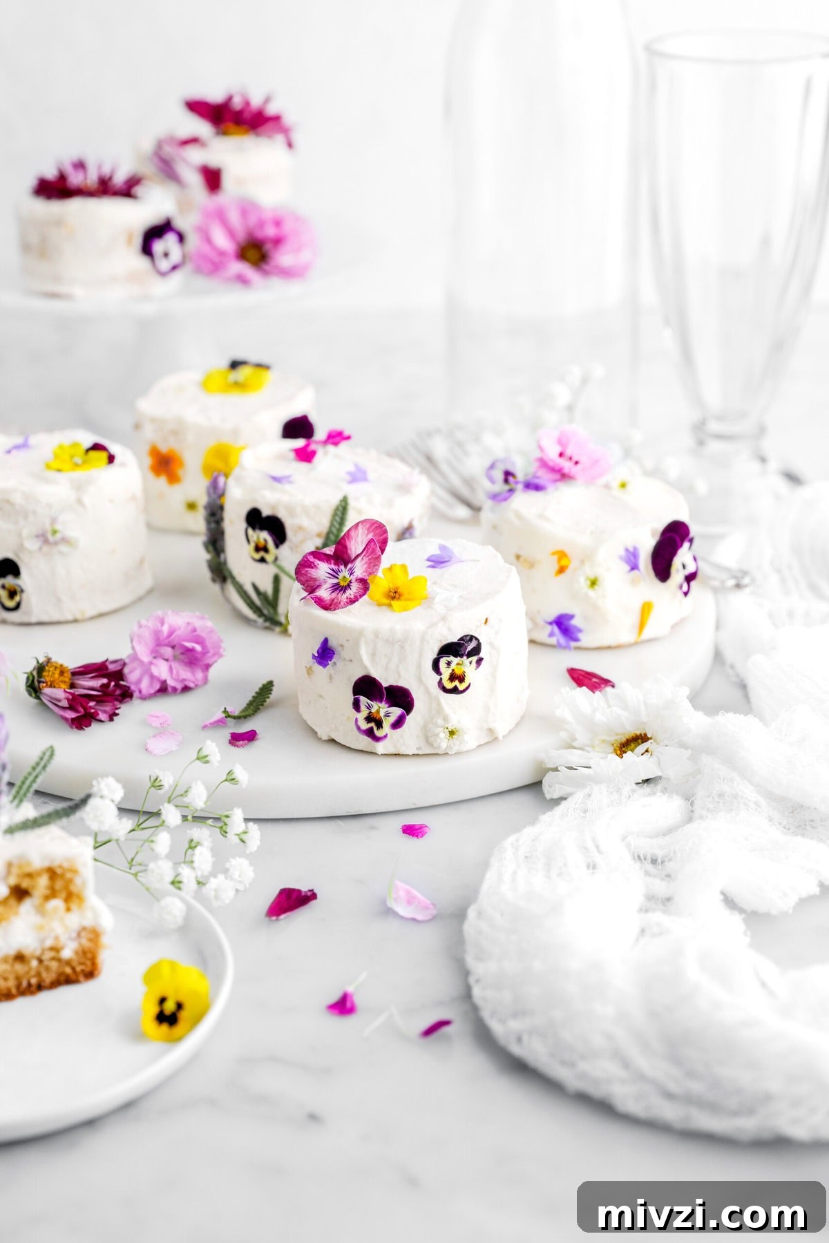 mini cakes on marble surface decorated with edible flowers.