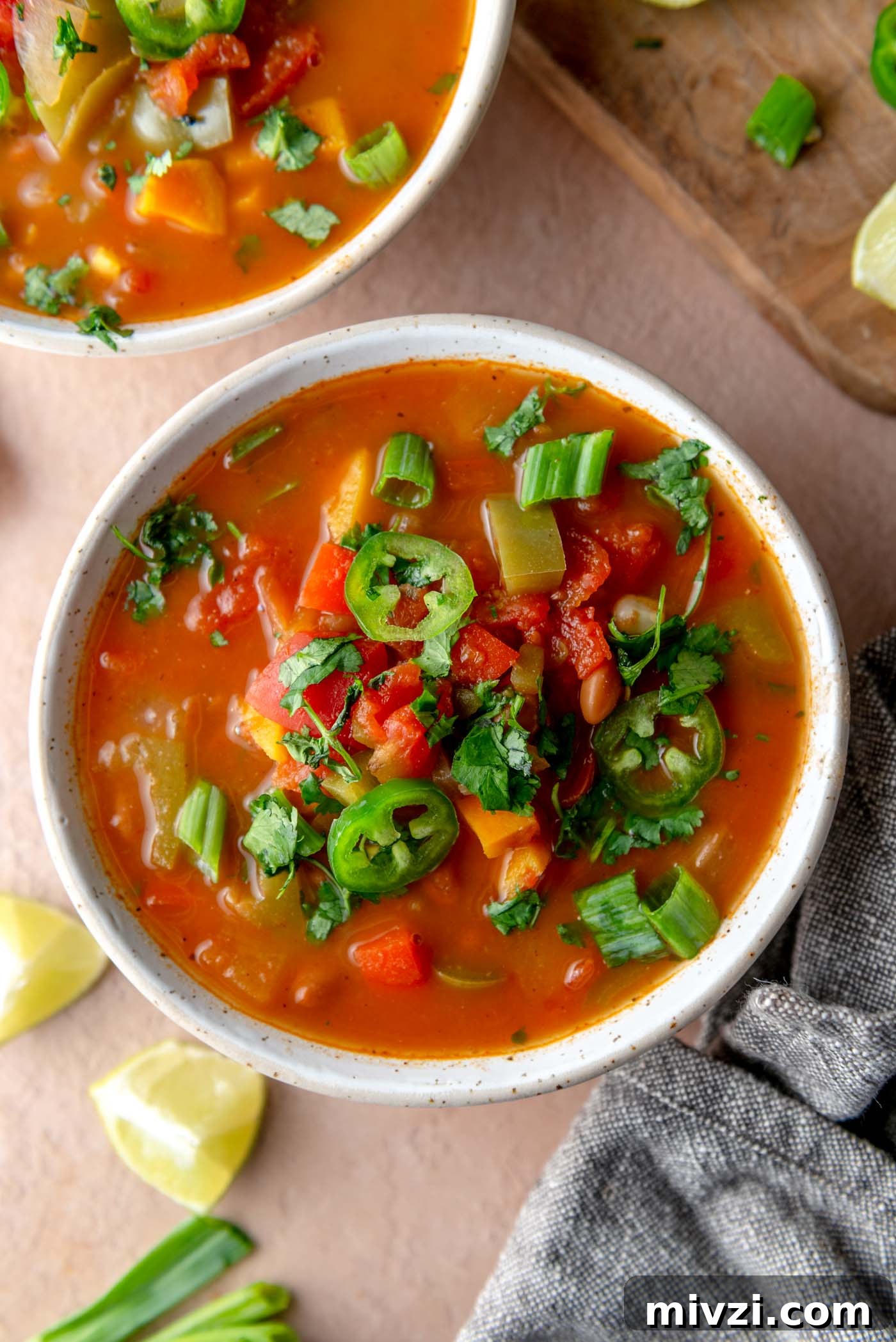 Hearty Vegan Enchilada Soup with Black Beans and Corn 2 Bowl of vegetarian enchilada soup with pinto beans, sweet potato, bell peppers, topped with cilantro, green onion and jalapeno slices.