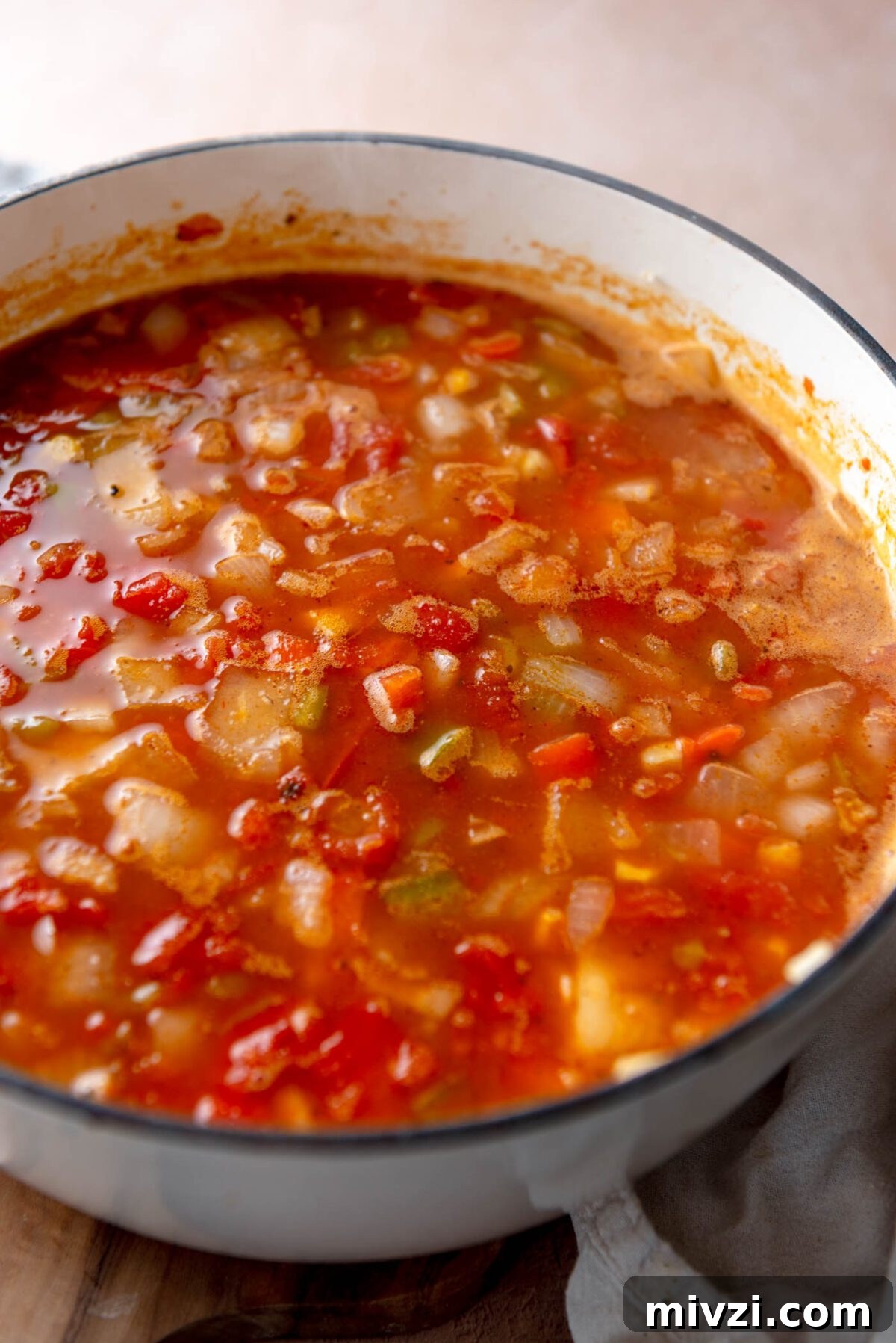 Hearty Vegan Enchilada Soup with Black Beans and Corn 6 Onion, bell pepper and beans cooking in a tomato-based broth in a soup pot.