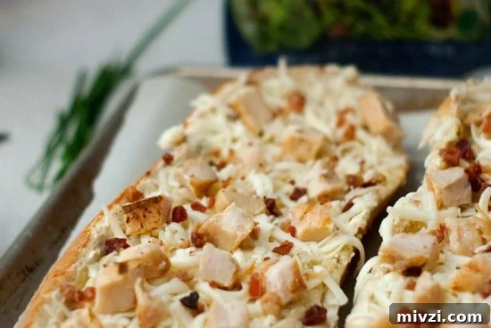 Garlic Bread Pizza with Chicken and Crispy Bacon 4 Garlic bread with with shredded mozzarella cheese, cooked chicken, and crumbled bacon on a baking sheet with parchment paper.