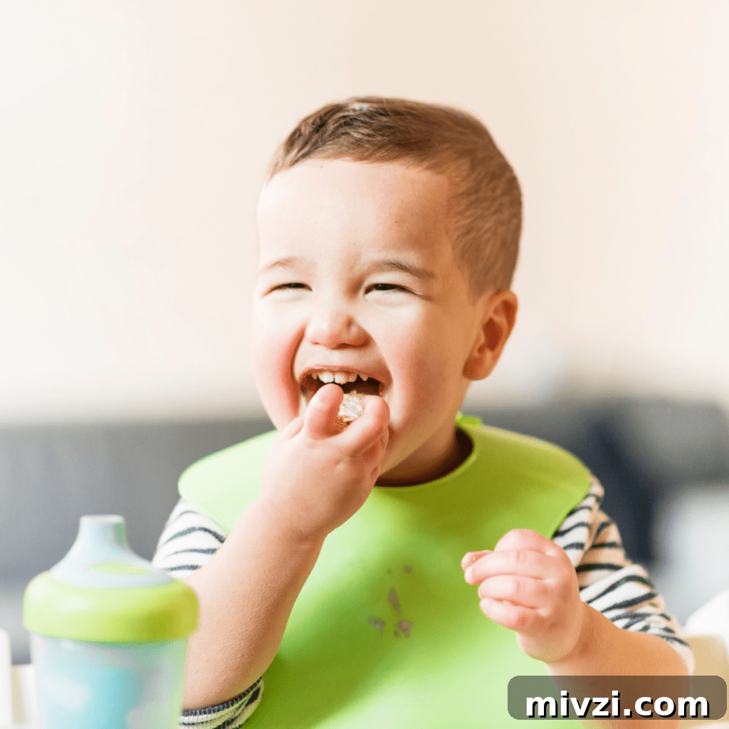 Toddler boy eating happily with a green bib.