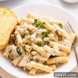 A plate of crockpot chicken alfredo with a piece of garlic bread on the side.