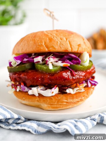 A sandwich with a sauce covered vegan patty, pickles, and coleslaw between two buns.