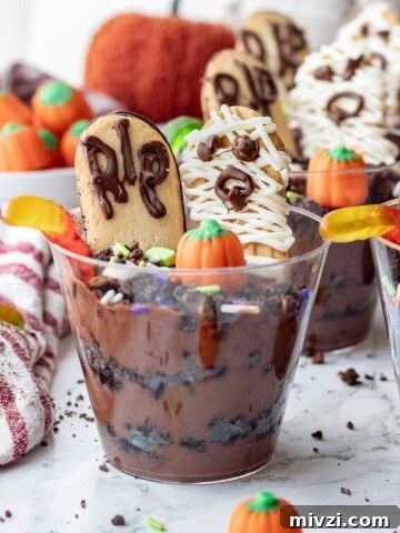 Clear cup of pudding and oreos with worms, pumpkin candy, sprinkles, headstone cookie, and mummy cookie.