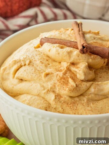 Whipped pumpkin cream cheese dip in white bowl with cinnamon sticks.