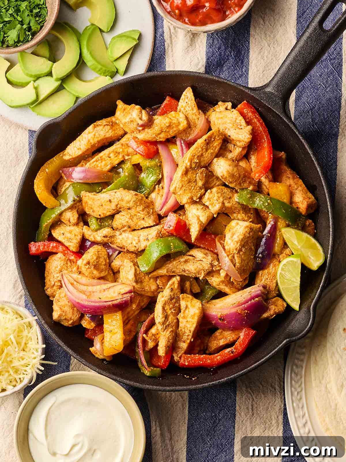 A pan on a set dinner table, filled with cooked fajitas, ready to serve up with side dishes.