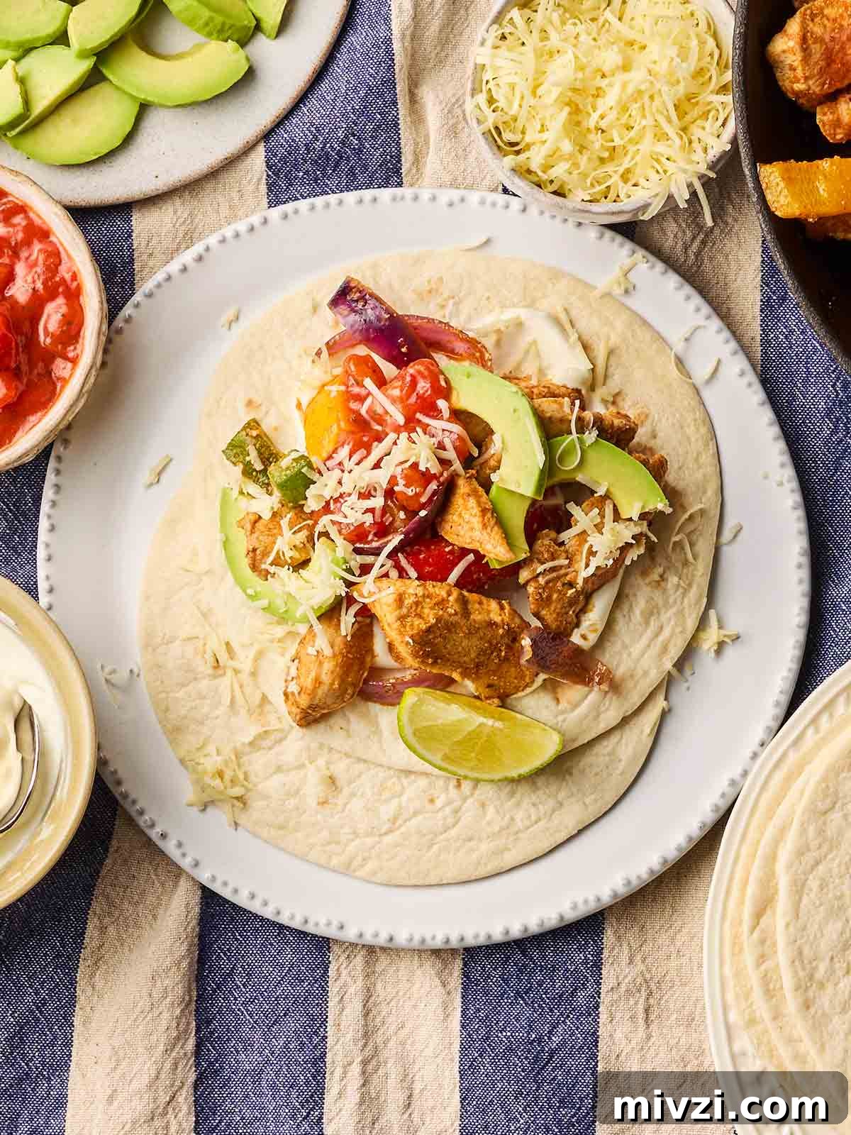 A plate of chicken fajitas in a wrap with lots of toppings, with lots of side dishes surrounding the plate, ready to eat.
