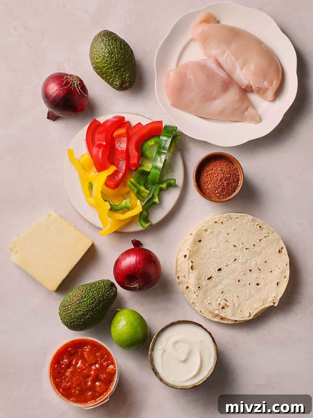 The raw ingredients for making chicken fajitas laid out on a white surface.