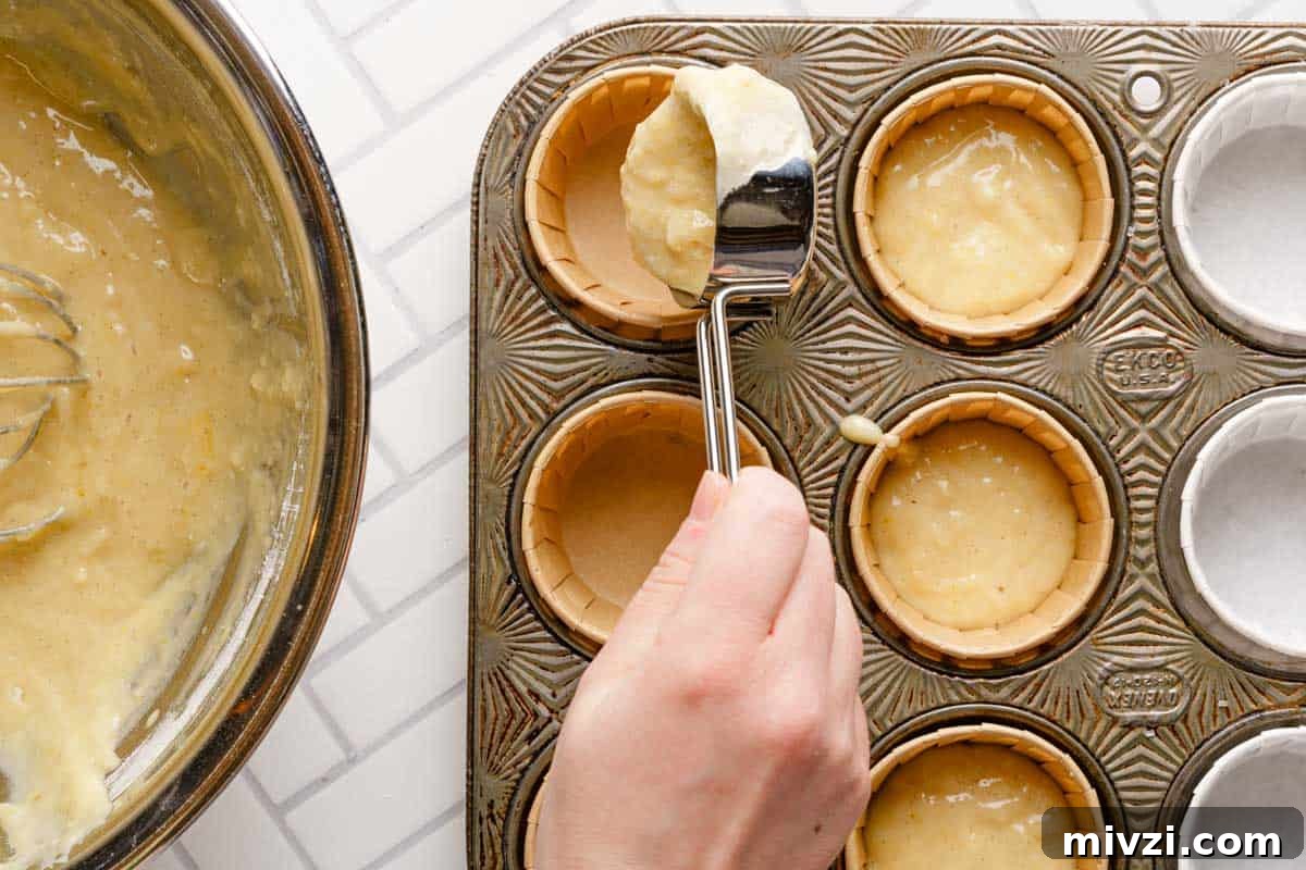 Classic Vanilla Muffins Recipe: Light, Fluffy & Quick 13 scoop of muffin batter being added to muffin tin.