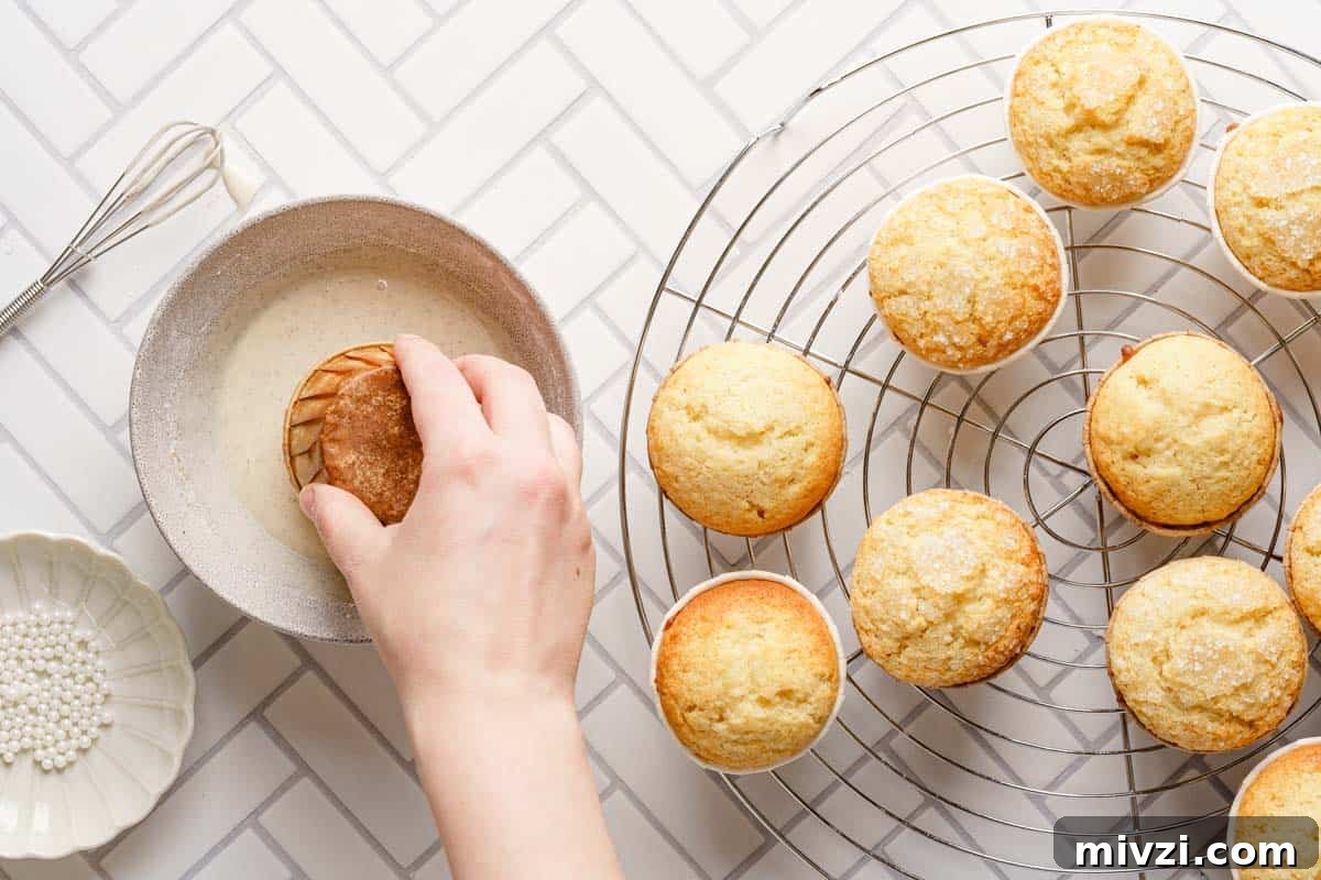 Classic Vanilla Muffins Recipe: Light, Fluffy & Quick 17 muffin being dipped into bowl of glaze with wire rack of muffins on the side.