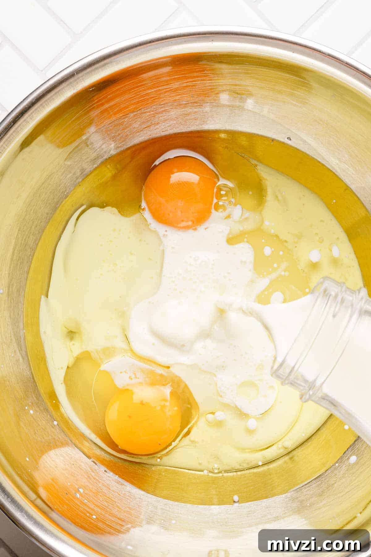 Classic Vanilla Muffins Recipe: Light, Fluffy & Quick 8 milk being poured into bowl with eggs and oil inside.