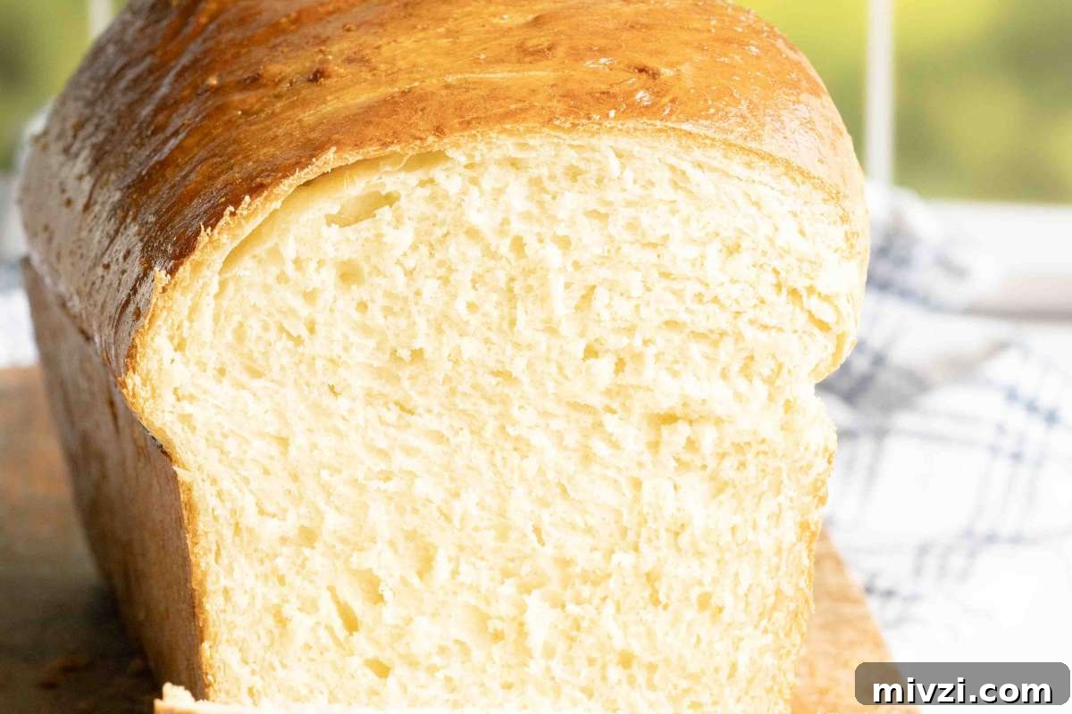 Horizontal view of a golden potato bread loaf on a cutting board, partially sliced to reveal its soft interior.