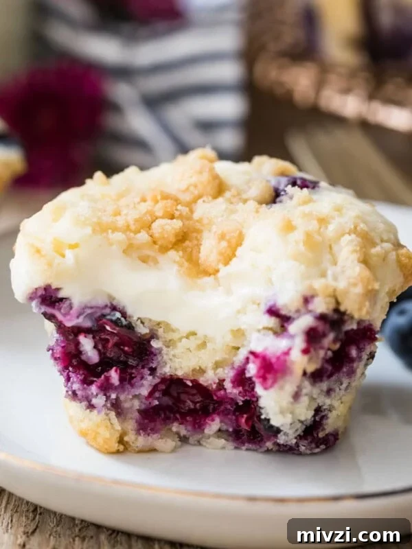 Closeup of blueberry cream cheese muffin with a bite taken out of it on a white plate.