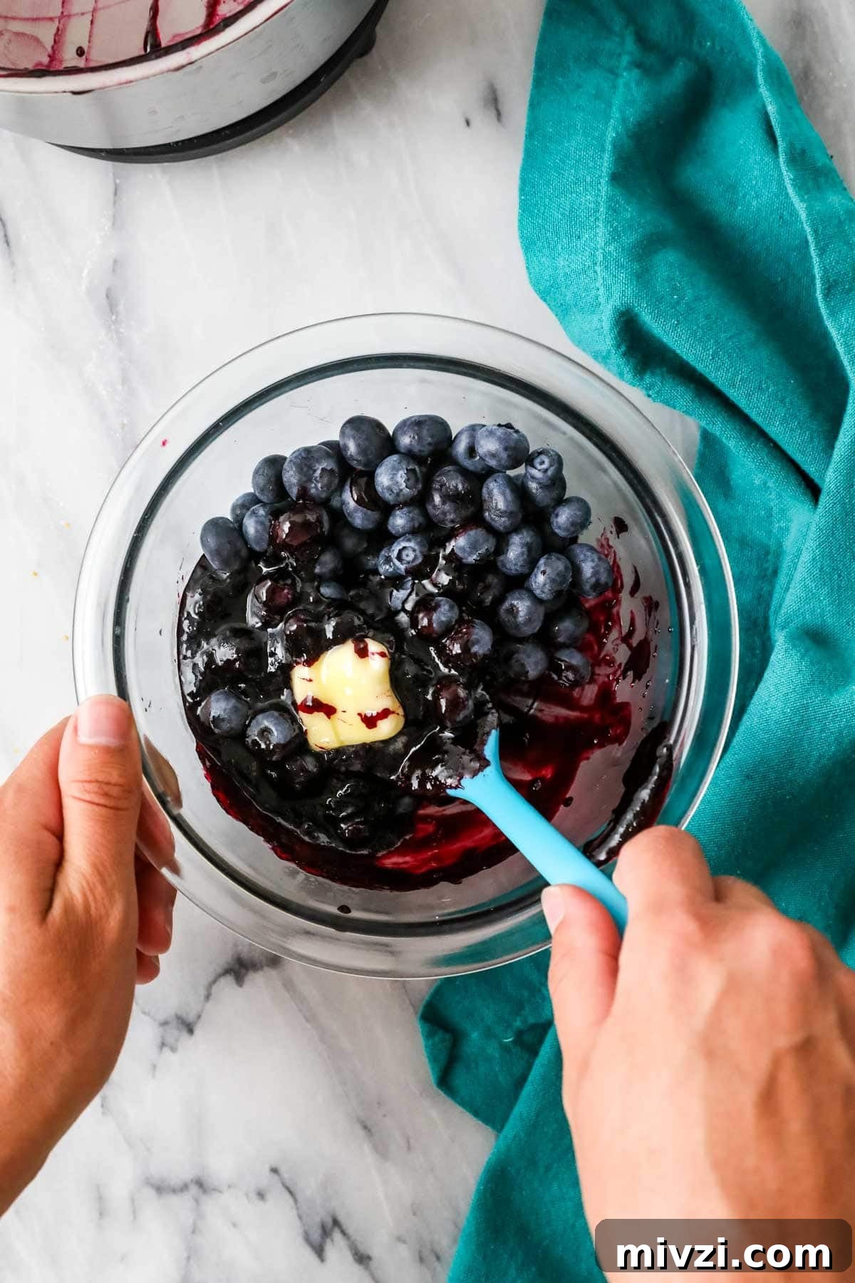 Butter and fresh blueberries being stirred into a cooked blueberry sauce mixture.