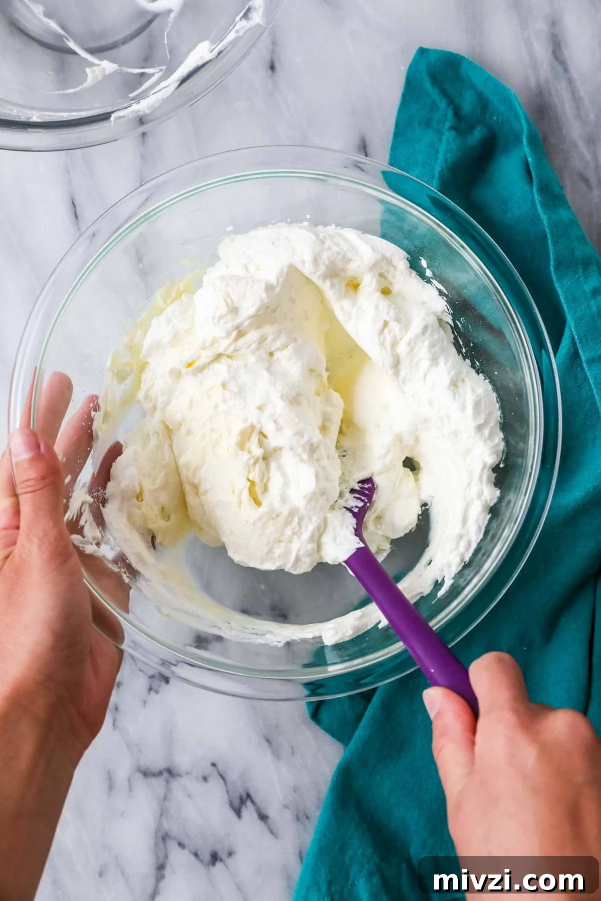 Spatula folding whipped cream into a cream cheese mixture.