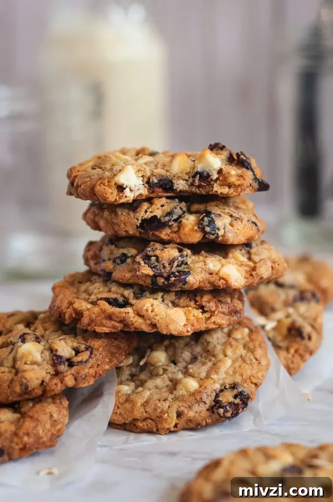 Chewy Oatmeal Coconut Chocolate Chip Cookies Recipe 9 A messy short stack of oatmeal cookies on a piece of white parchment paper full of dried cherries and white chocolate chips.