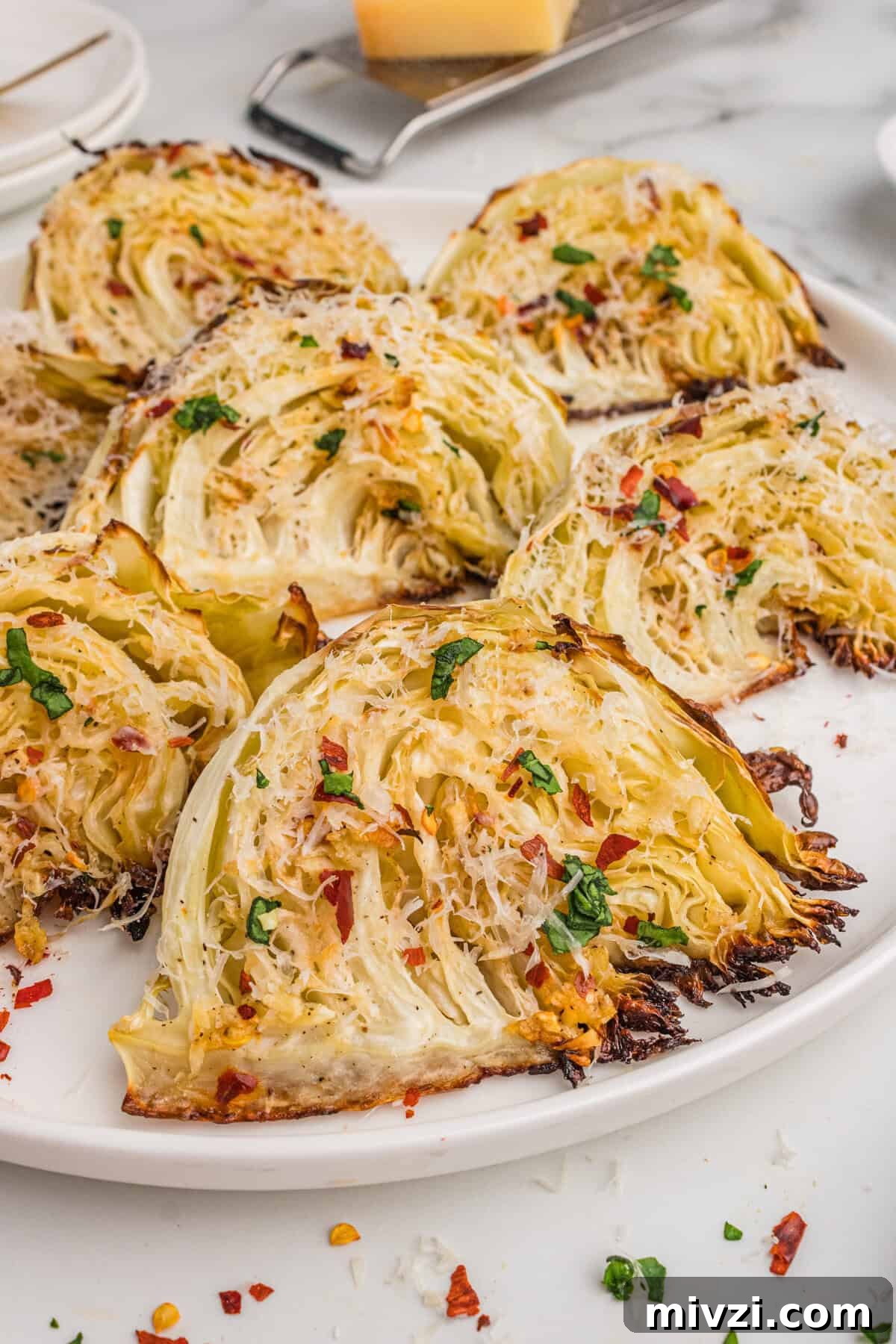 Crispy Roasted Cabbage Wedges with Garlic and Parmesan 2 Roasted cabbage wedges with garlic, Parmesan cheese, and red pepper flakes, served on a white plate.