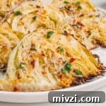 Crispy Roasted Cabbage Wedges with Garlic and Parmesan 12 Close-up of roasted garlic parmesan cabbage wedges on a white plate, with golden brown edges, shredded parmesan, parsley, and red pepper flakes.