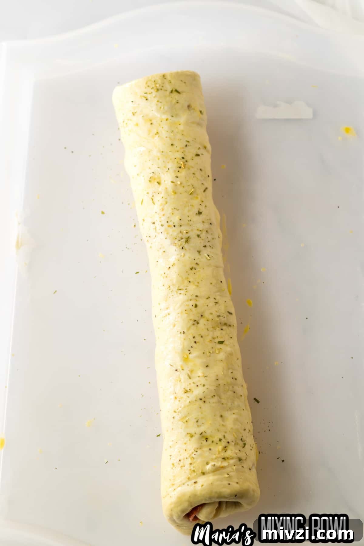 Pepperoni-Stuffed Bread: Cheesy, Savory Pull-Apart Loaf 7 roll of stuffed pepperoni bread on a parchment baking sheet being brushed with egg wash and seasoned with italian seasoning.