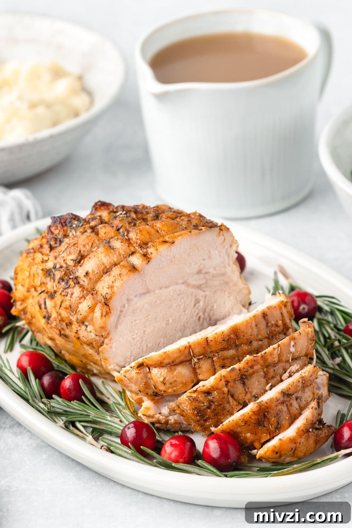 Roast chicken with herbs garnished with cranberries and rosemary on a white platter.